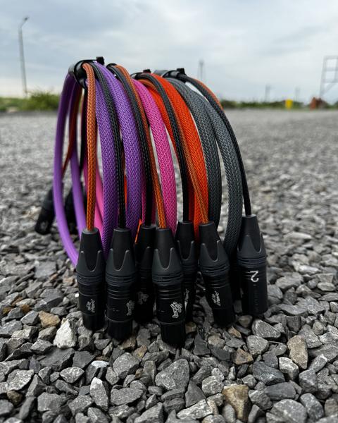 Kolorowe kable XLR z grawerowanymi laserowo wtykami ustawione na żwirze